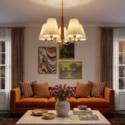 Metal dining room chandelier hanging above a warm living room seating area with an orange sofa and layered wall art.