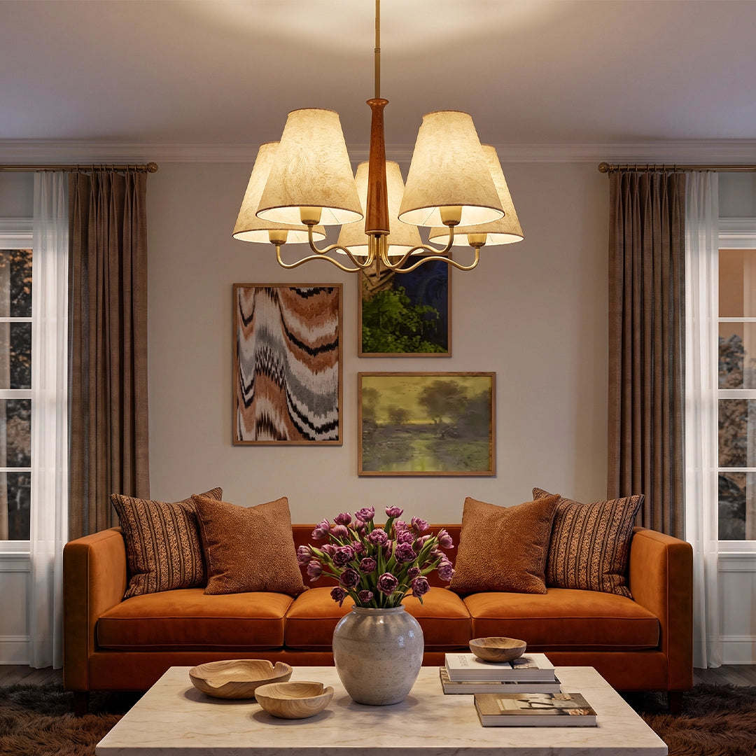 Metal dining room chandelier hanging above a warm living room seating area with an orange sofa and layered wall art.