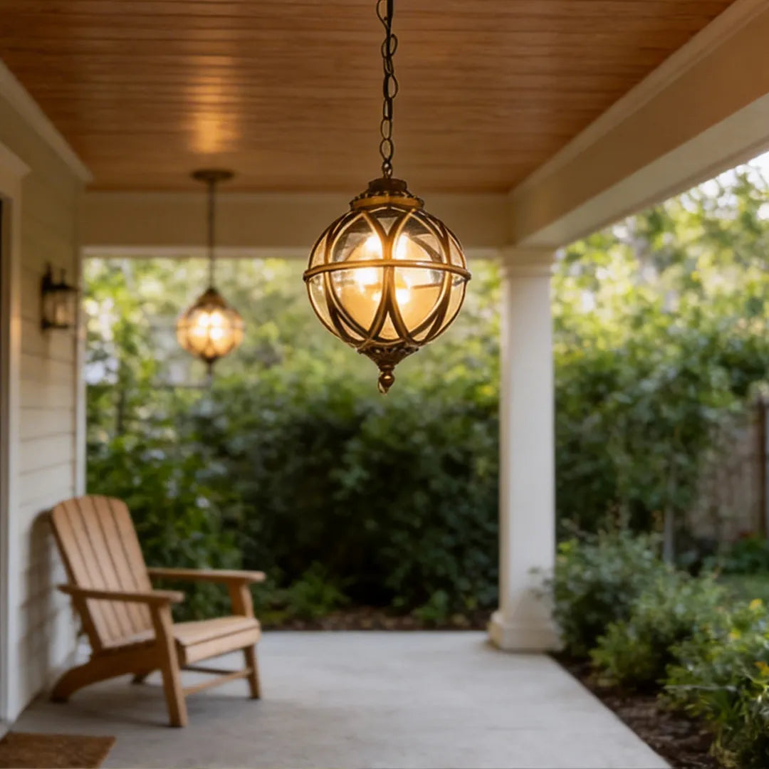 Metal orb pendant light illuminating a covered porch with wood ceiling and wooden lounge chair.