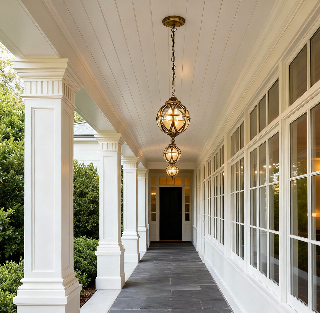 Metal orb pendant light hanging along a covered porch hallway, providing warm and elegant outdoor ceiling illumination.