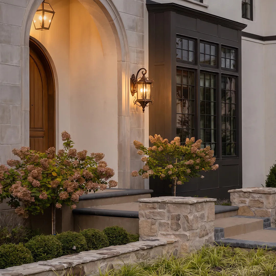 Metal outdoor wall sconce installed beside a stone archway entry, featuring an ornate lantern frame and warm candle-style bulbs.