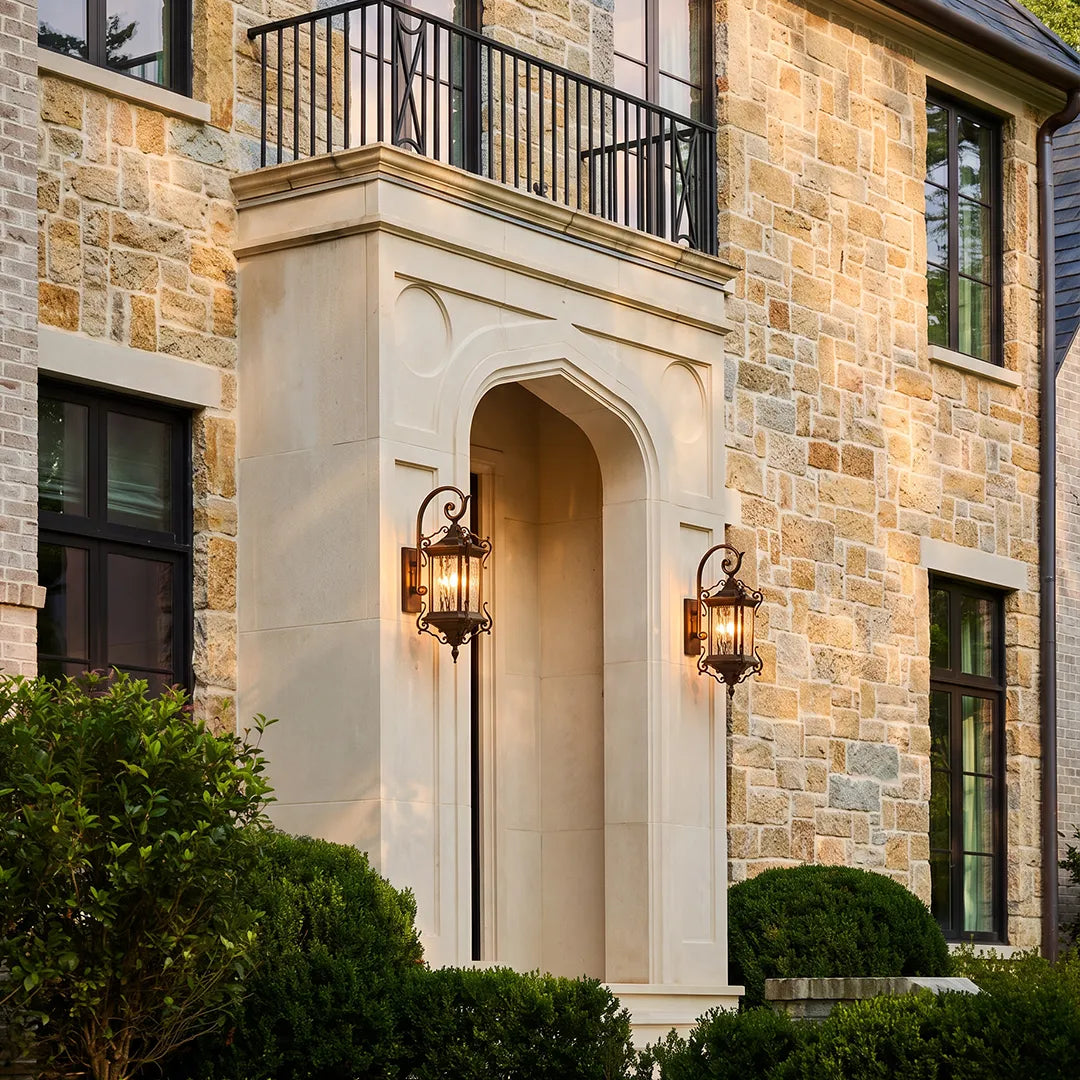 Metal outdoor wall sconces mounted around a grand stone entry porch, bringing classic lantern lighting to the exterior facade.