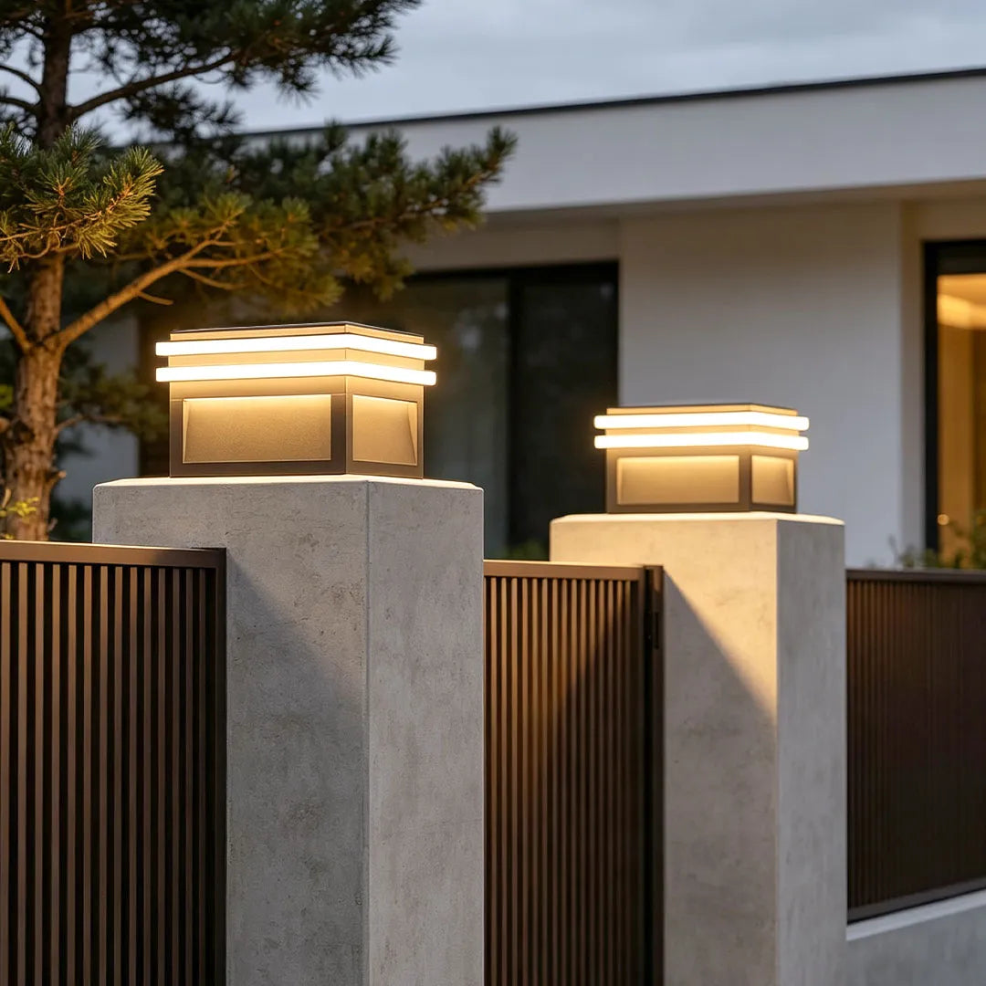 Metal pillar lights mounted on modern concrete posts along a contemporary outdoor fence.