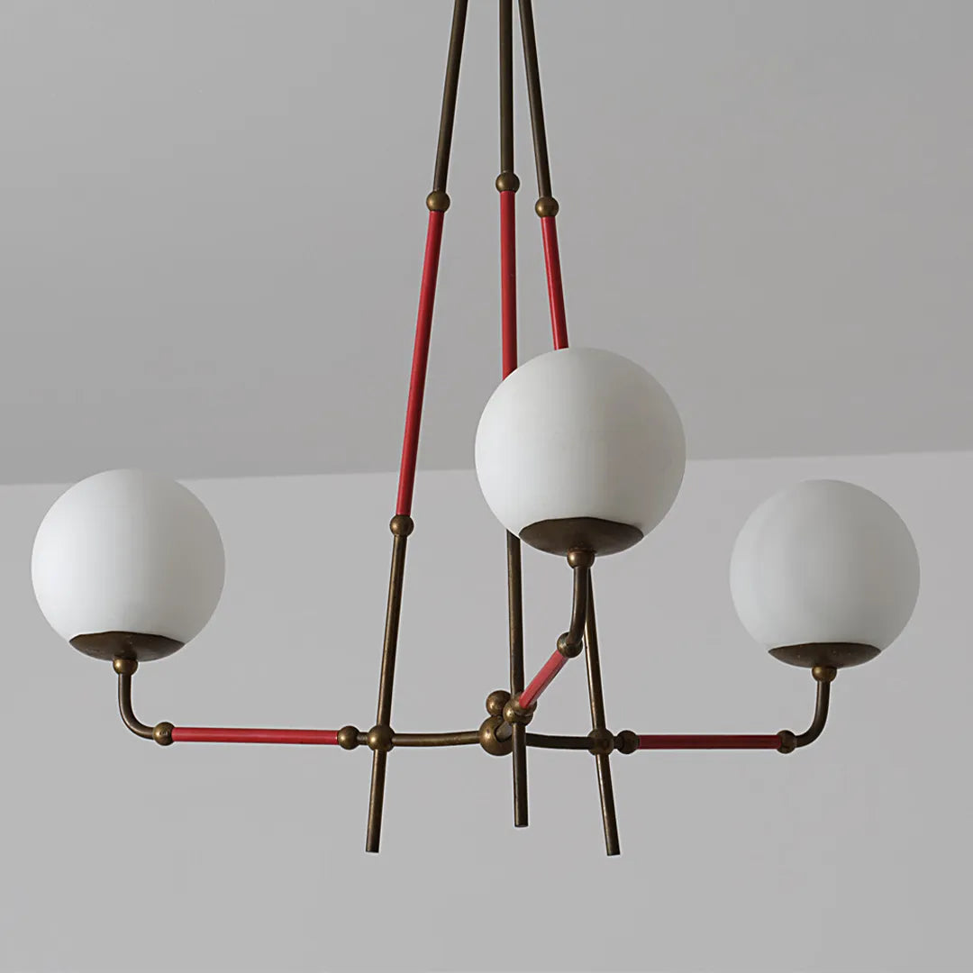 Mid century modern chandelier product close-up showing three white globe shades and red suspension cords.