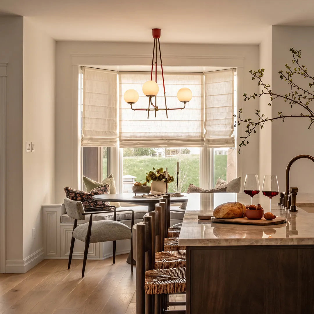Mid century modern chandelier hanging over a dining area beside a kitchen island and large window.