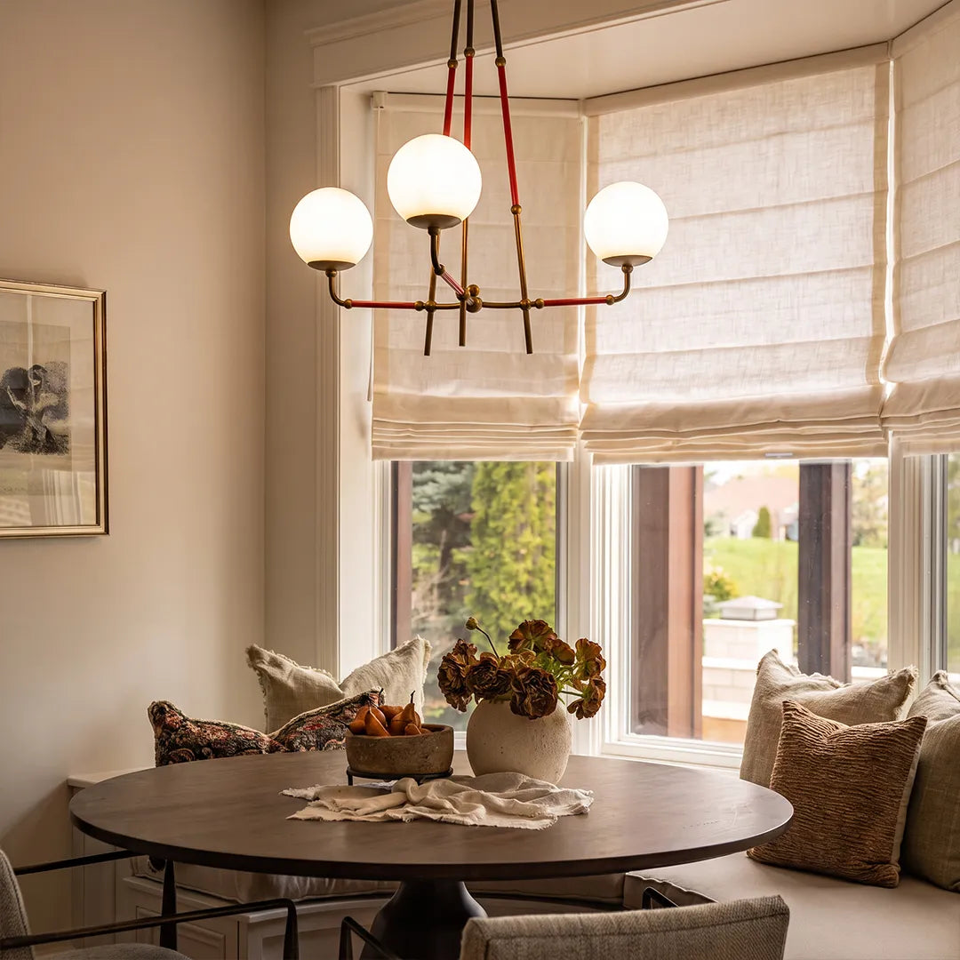 Mid century modern chandelier suspended over a round dining table beside a bright window nook.