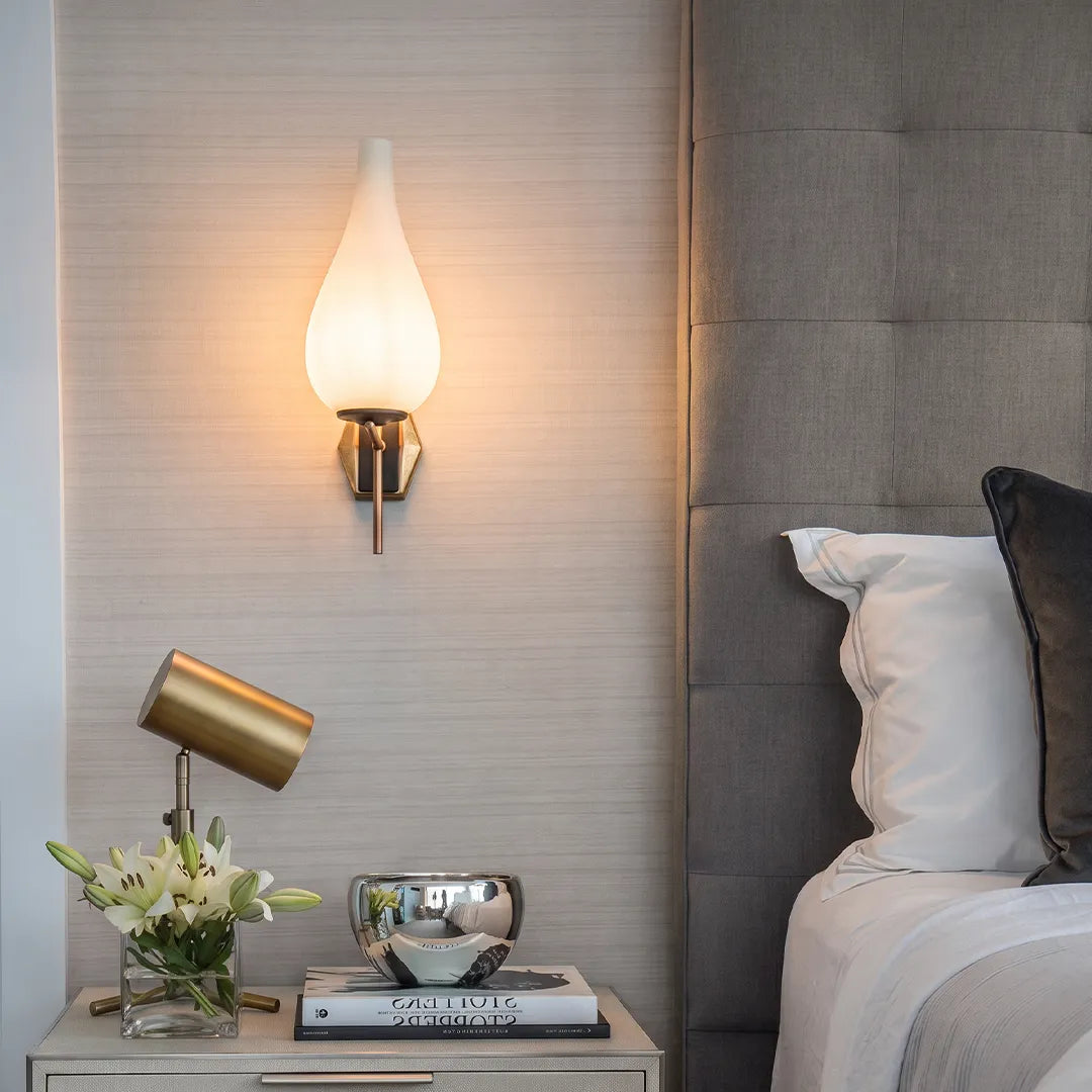 Mid century modern wall light installed above a bedside console with a glowing frosted glass shade.