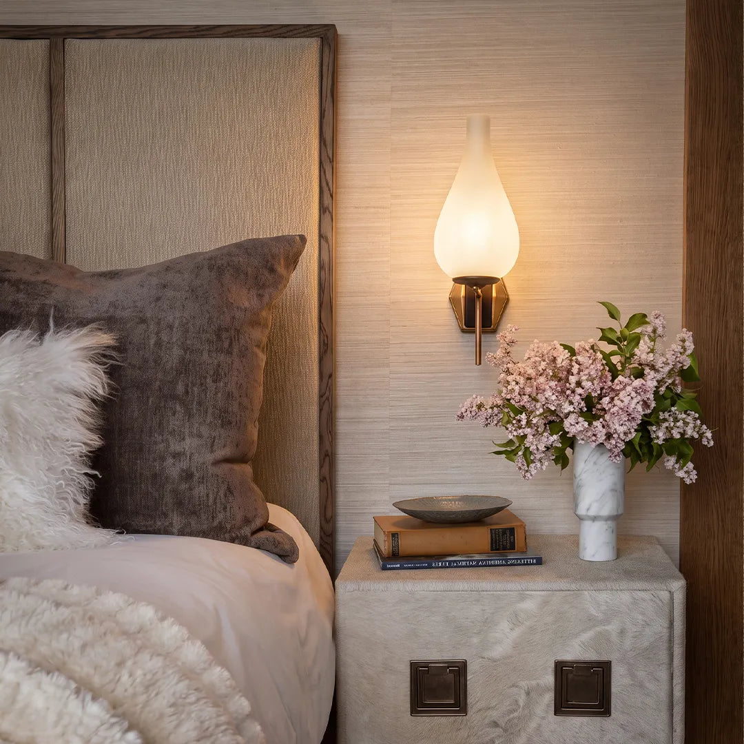 Mid century modern wall light above a bedside table with a warm frosted glass shade and brass finish.Mid century modern wall light above a bedside table with a warm frosted glass shade and brass finish.