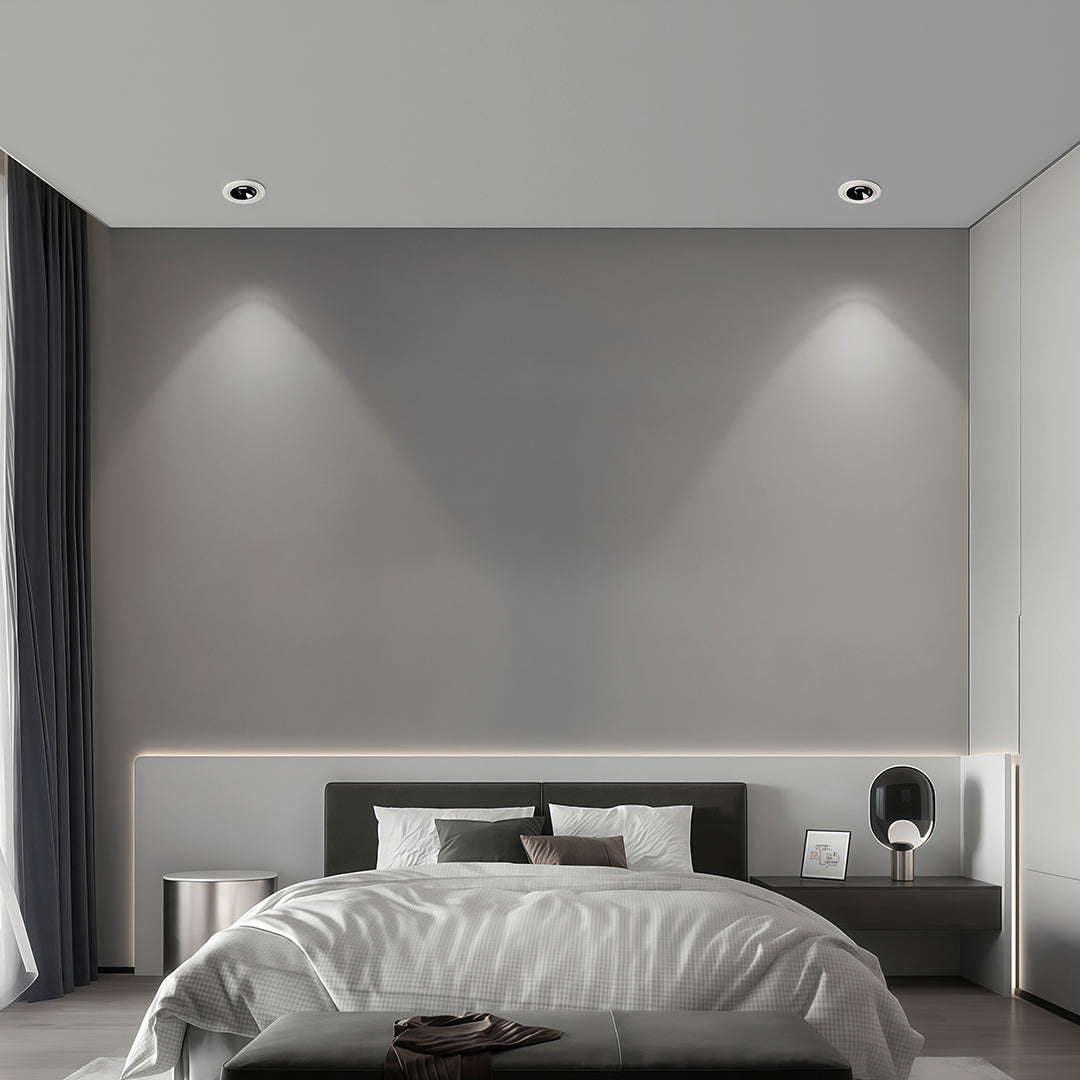 Minimalist bedroom with directional recessed downlight fixtures creating a wall-wash effect over the headboard.