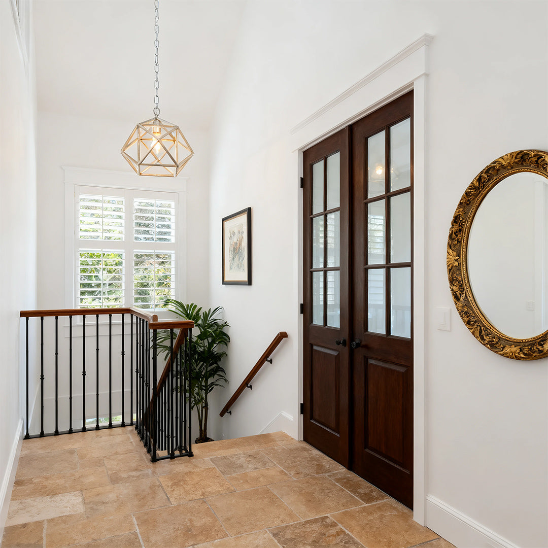 Minimalist gold metal pendant light centered in a bright, white-walled hallway with dark wood french doors and natural light.