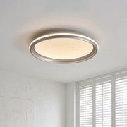 Minimalist metal flush mount light with a silver ring frame and a warm textured glowing shade.