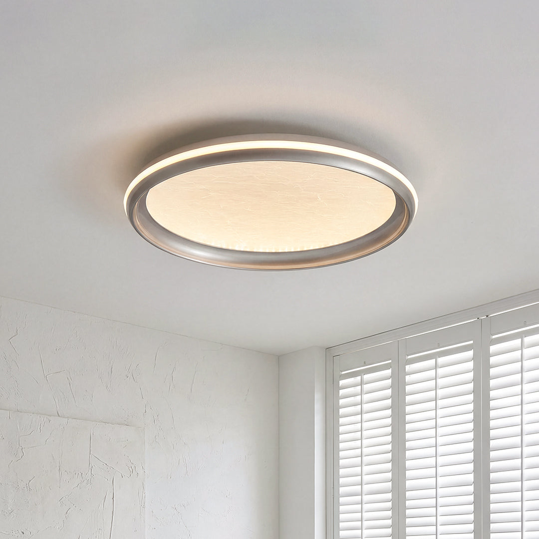 Minimalist metal flush mount light with a silver ring frame and a warm textured glowing shade.