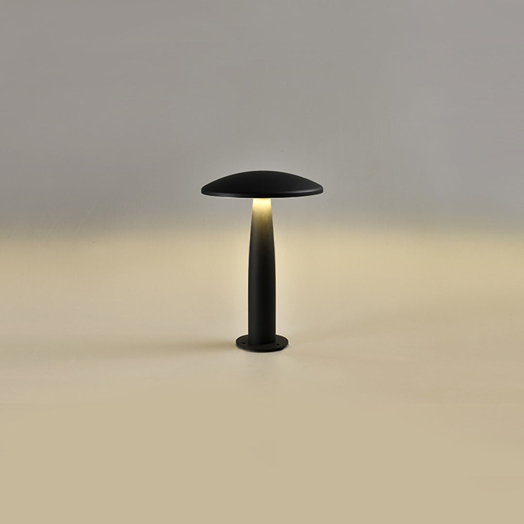 Black mushroom bollard light standing alone, casting a warm glow in a minimalist outdoor setting.