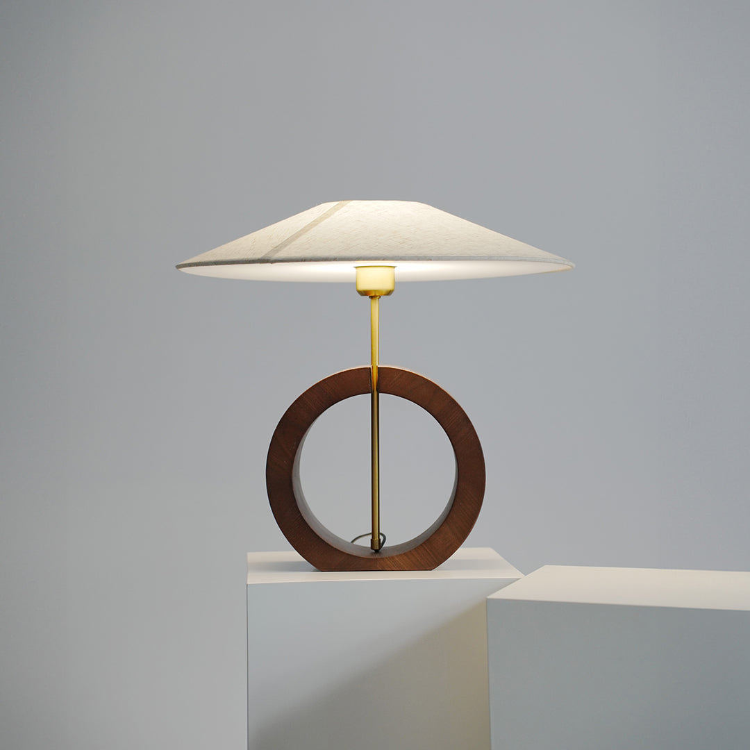 Minimalist natural wood table lamp glowing softly in dark background.