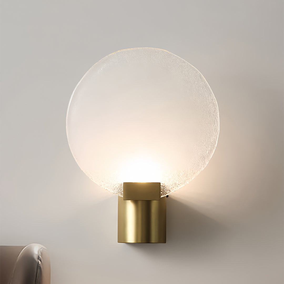 Minimalist round wall light with a frosted glass shade and gold base, casting a soft glow in a modern bedroom.