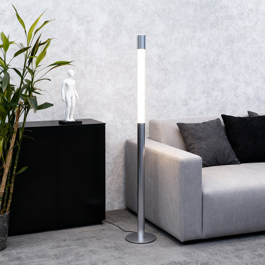 Minimalist silver Italian floor lamp standing beside a contemporary grey sofa and black console cabinet. 