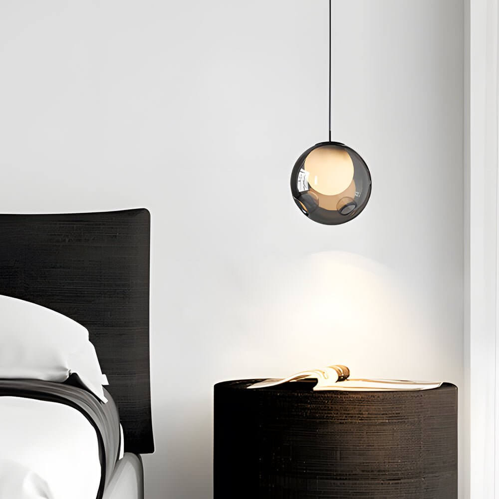Minimalist smoked glass pendant light hanging over a black bedside nightstand in a tidy bedroom.