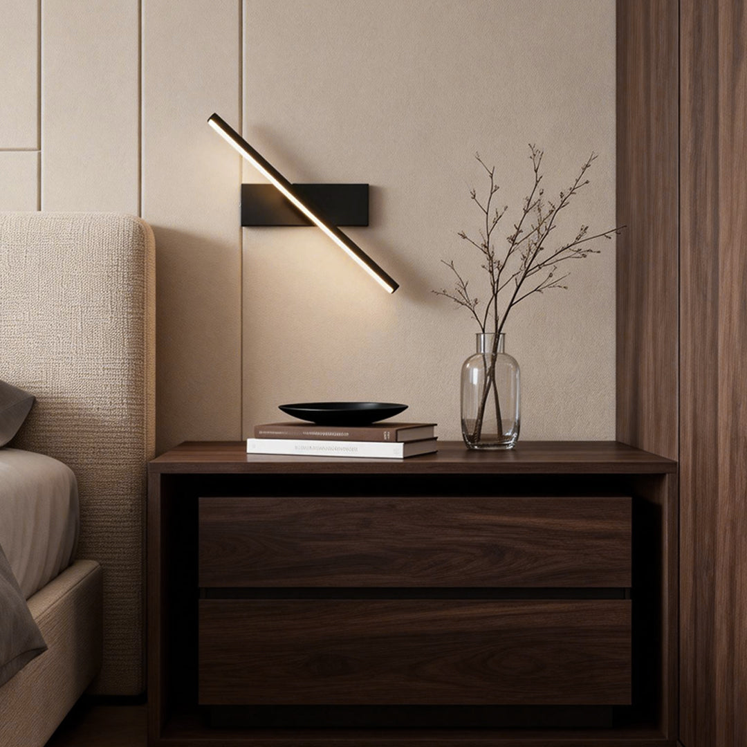 Modern minimalist swivel wall light with sleek black and gold design, mounted above a wooden nightstand in a cozy bedroom.
