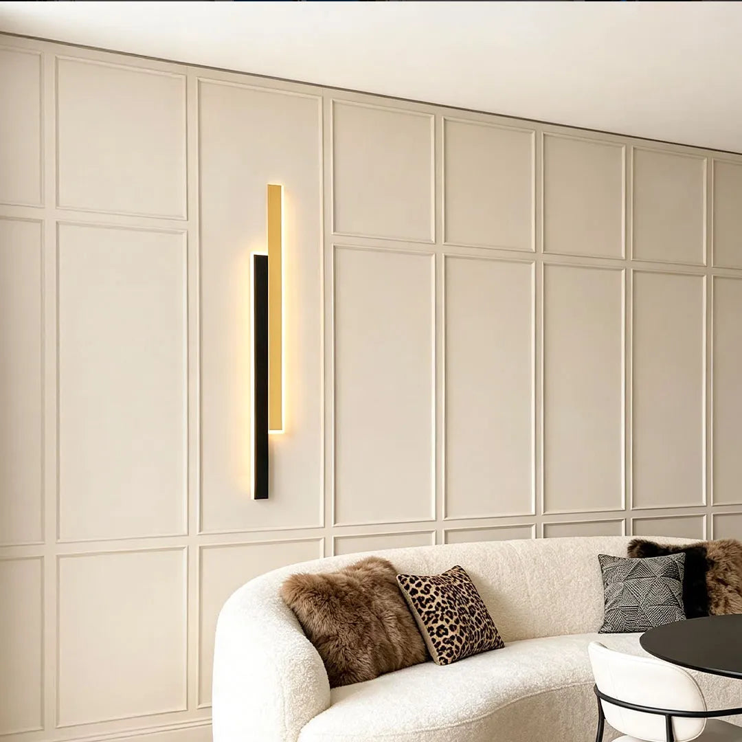 Minimalist vertical wall light above a cream sofa against paneled wall décor in a modern living room.