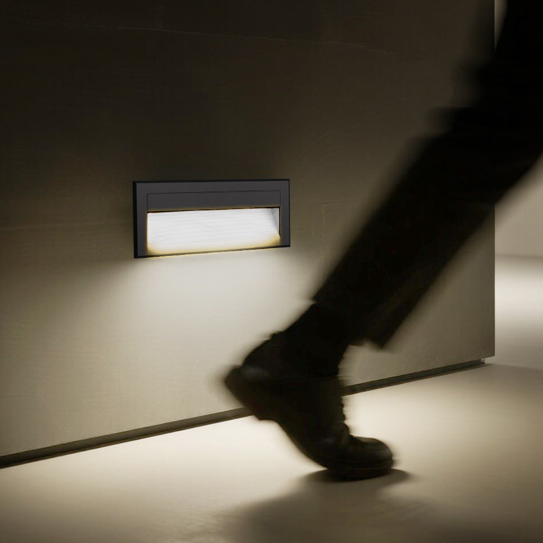 Minimalist wall-mounted step light illuminating decorative stone aggregate surface below