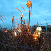 Golden and amber garden globe stakes producing warm illumination for decorative landscape lighting pathway.
