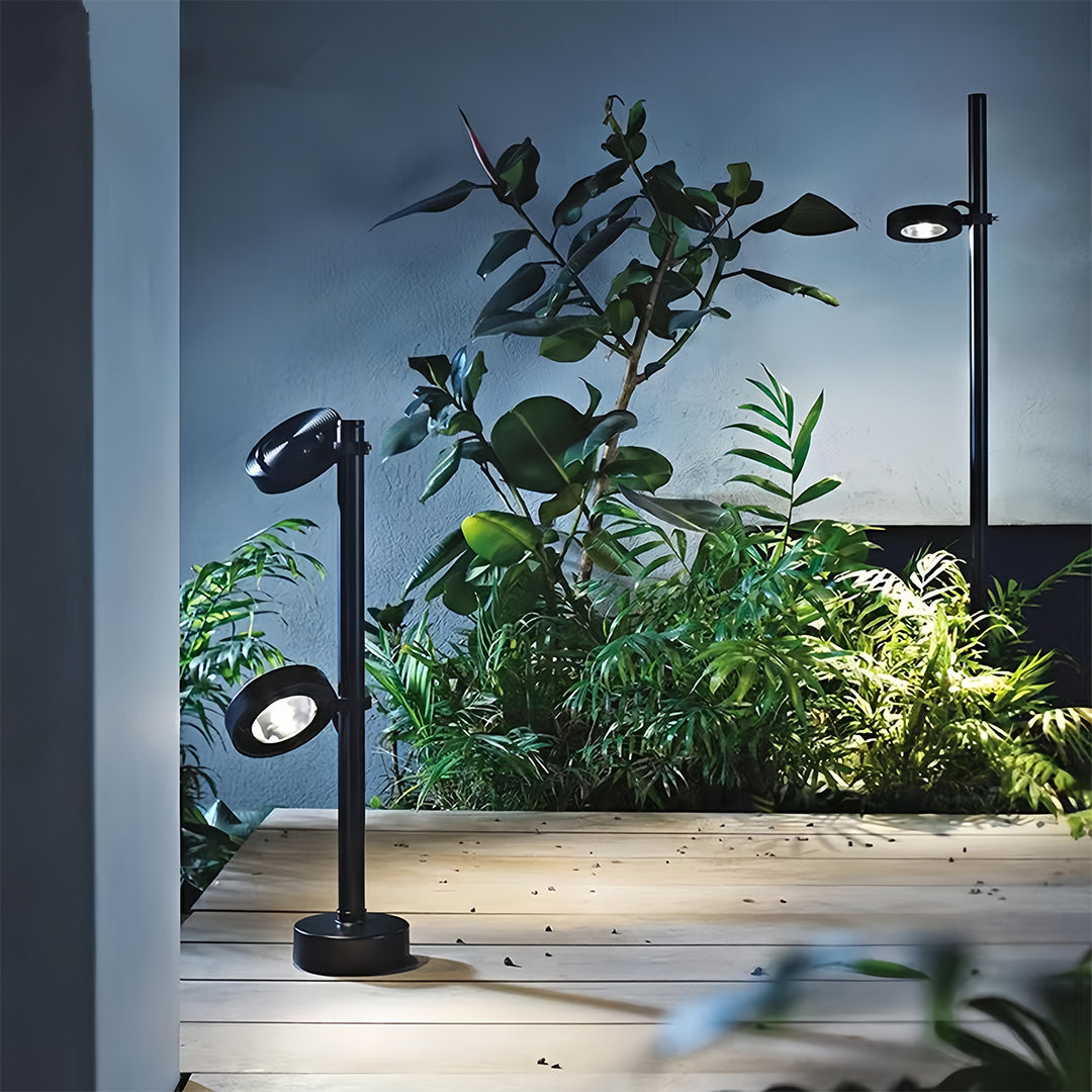 Modern adjustable pathway landscape lights installed next to a wooden deck, highlighting potted plants and creating warm accent lighting.