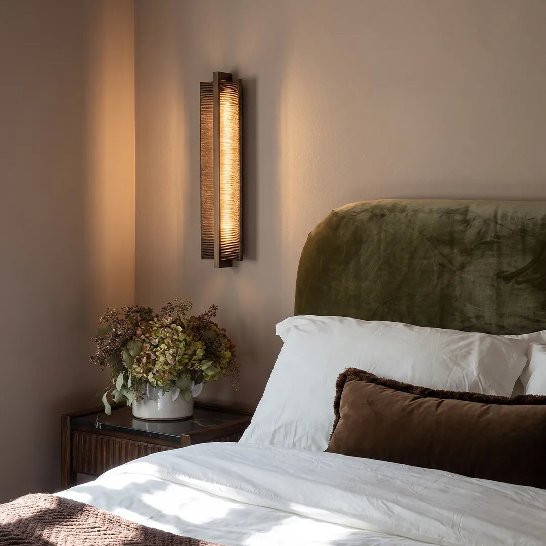 Modern bedroom with vertical wall sconce warm bedside lighting and neutral decor
