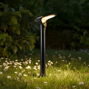 Modern black aluminum solar bollard lights illuminating a flower bed and grassy patch at night.