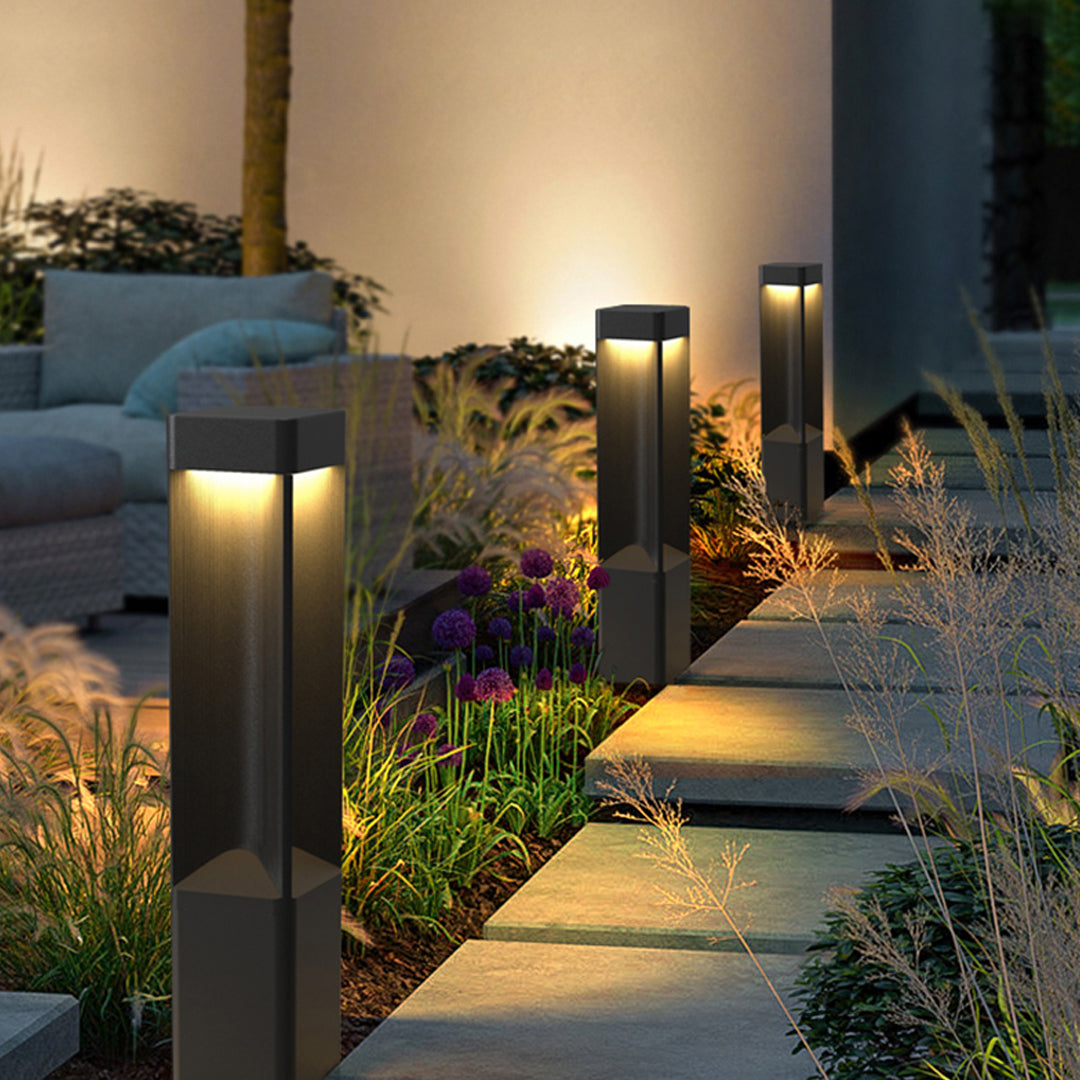 Modern black bollard lighting along a stone garden path with glowing warm led lights at night.