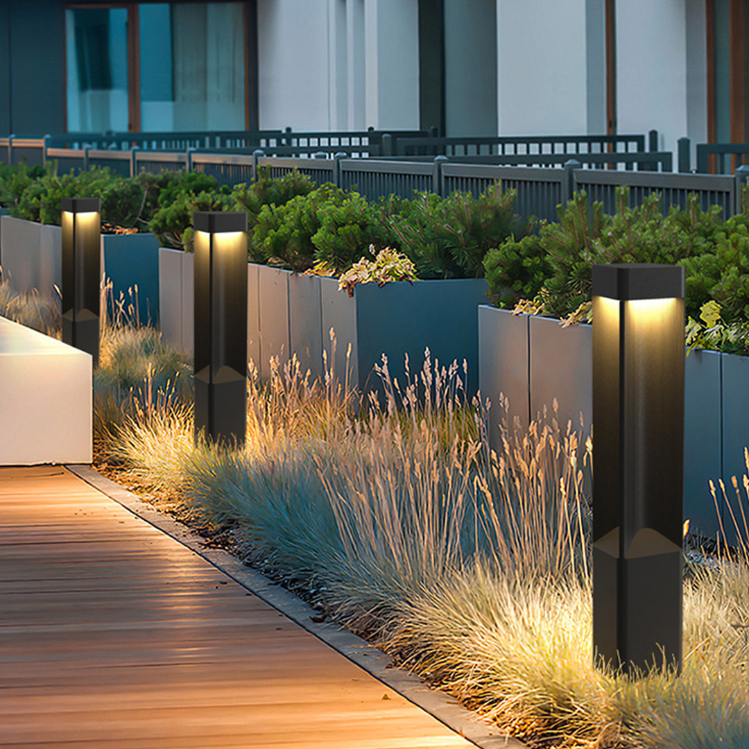 A row of modern black bollards lighting fixtures along a wooden walkway with warm LED glows now.