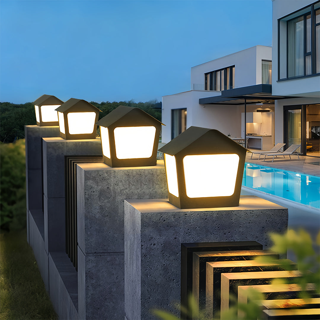 Modern black deck post cap lights lining a low concrete wall, brightly illuminating a poolside garden at twilight.