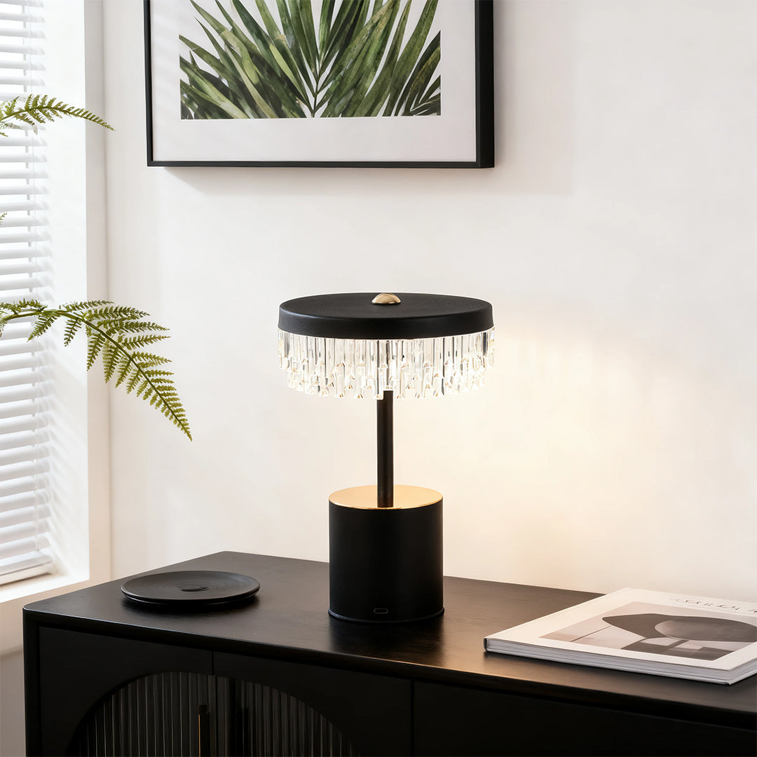 Modern black and gold fringe table lamp with layered crystal fringe, styled on a dark console cabinet.