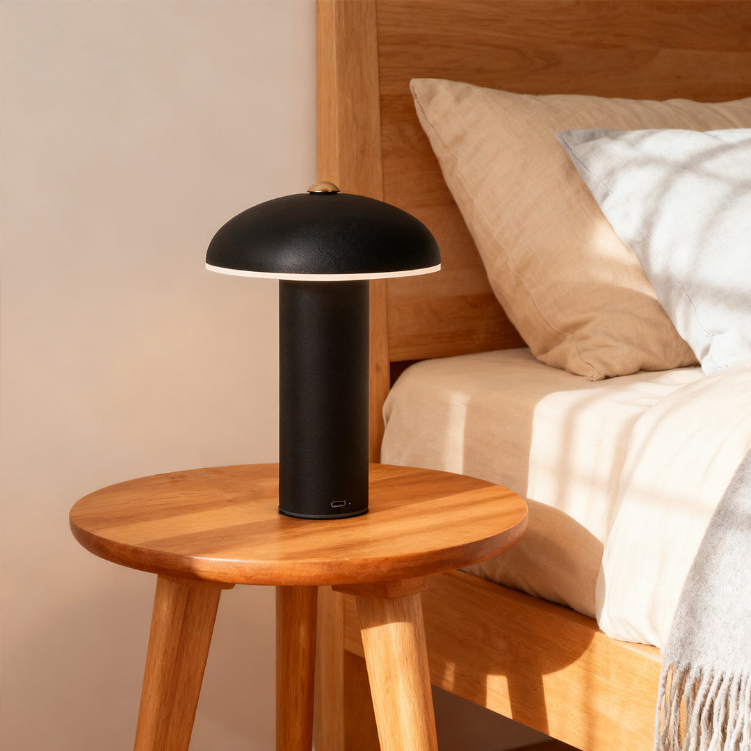 Modern black mushroom dimmable LED table lamp sitting on a round wooden bedside table in a cozy bedroom.