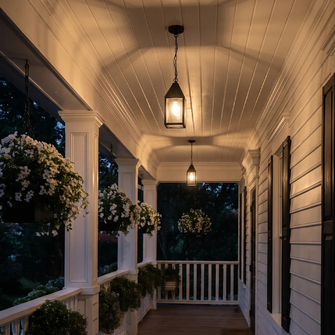 Modern black outdoor pendant light illuminating a long front porch at night with warm ambient exterior lighting.