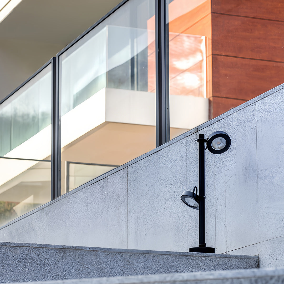 Modern black pole pathway landscape lights illuminating a concrete staircase and a building's glass facade in a clean, contemporary design.