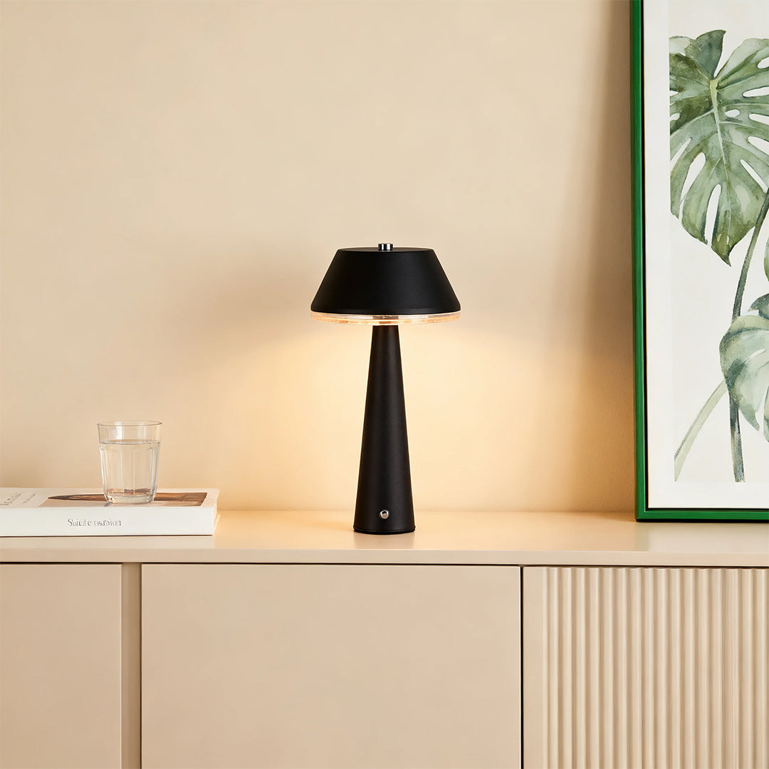 Modern black rechargeable table lamps casting warm light on a light wood sideboard beneath a tropical framed print. 