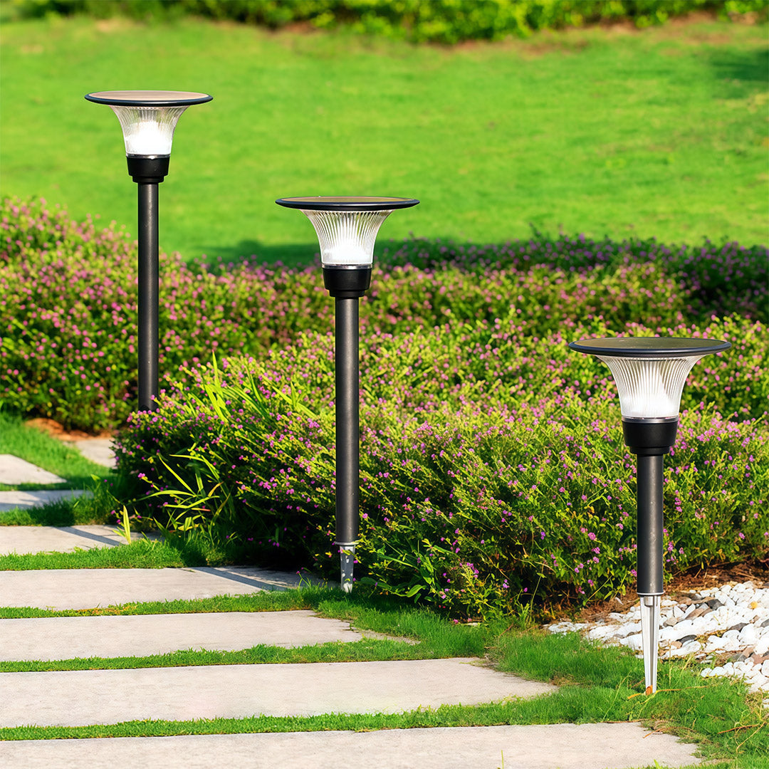 Modern black solar pathway lights with 'halo' solar panels staked in a garden next to a stone walkway.