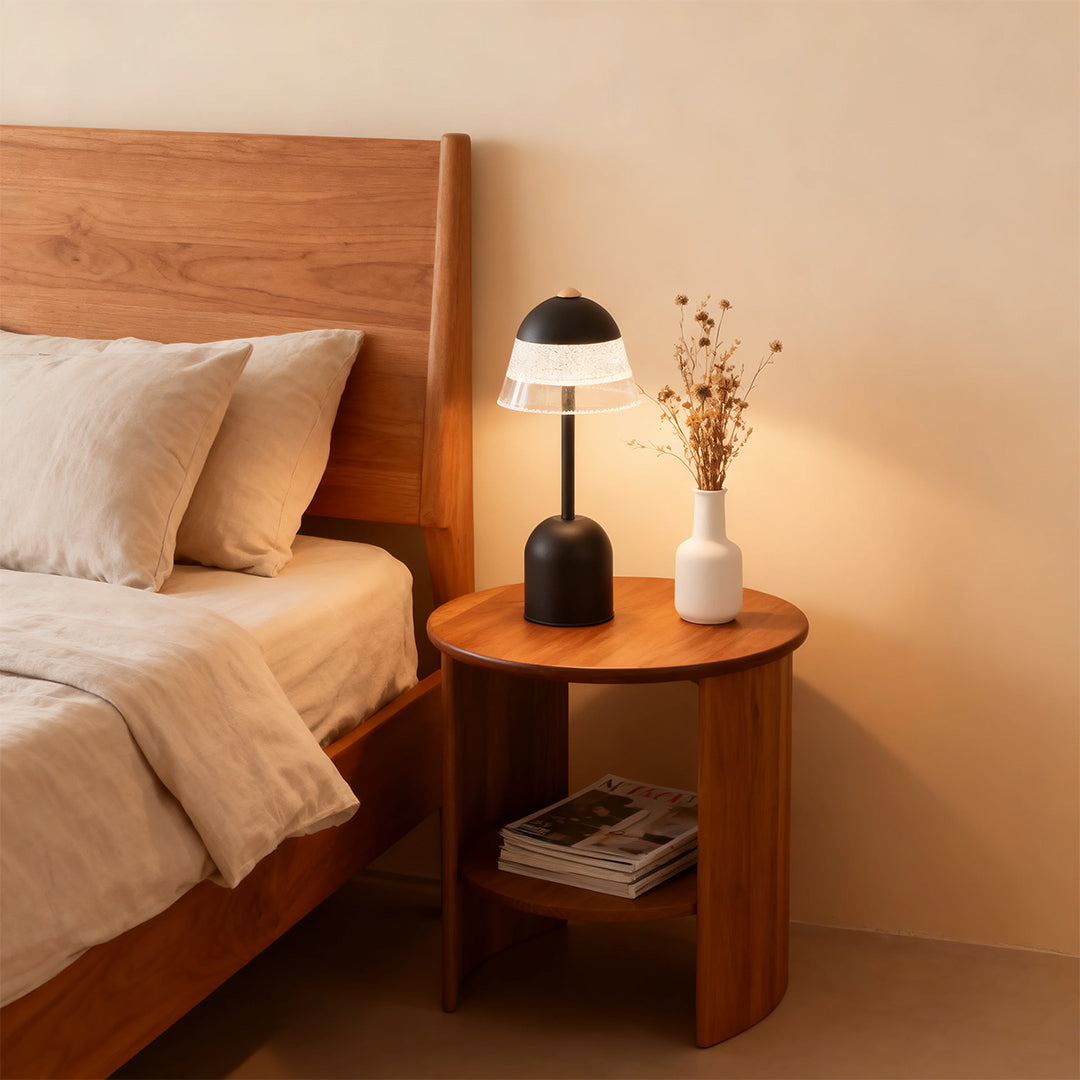 Modern black USB table lamps providing a warm bedside glow on a round wooden nightstand in a neutral bedroom.