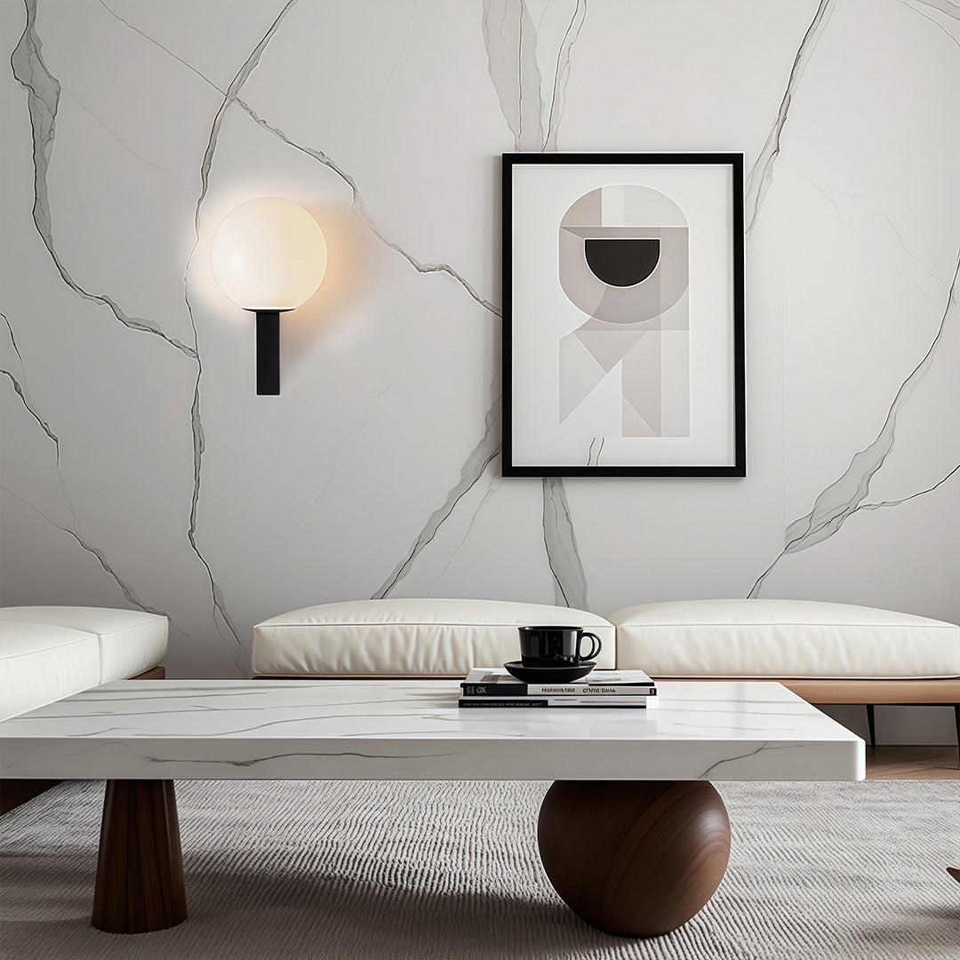 Modern black and white globe wall light mounted on a marble-textured wall above a low seating area in a minimalist room.