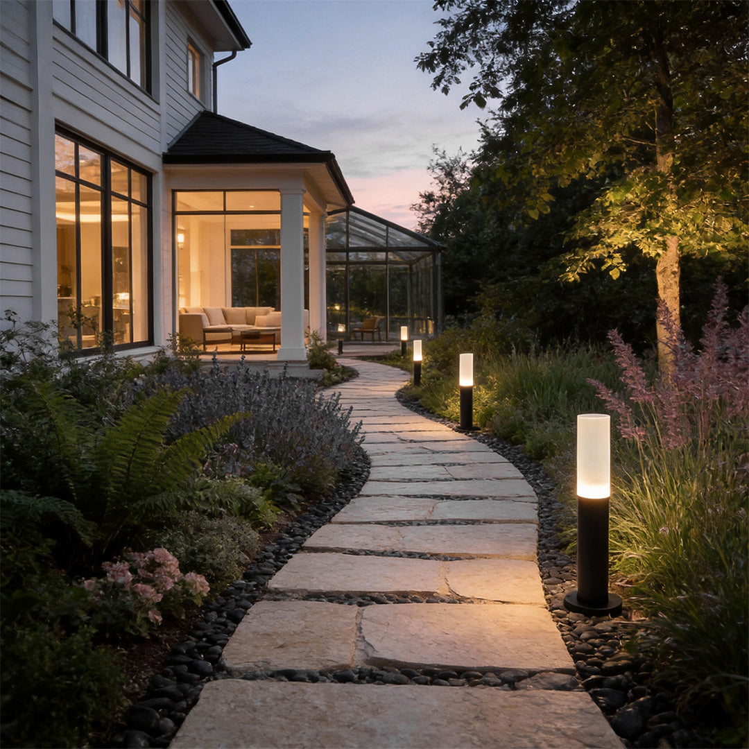 Modern bollard lighting providing soft light along a paved walkway with greenery.