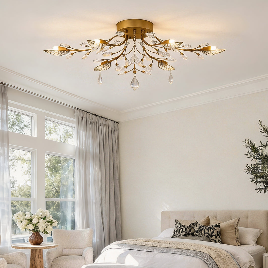 Modern branch chandelier with gold finish and crystal details installed in a bright bedroom with a sitting area.