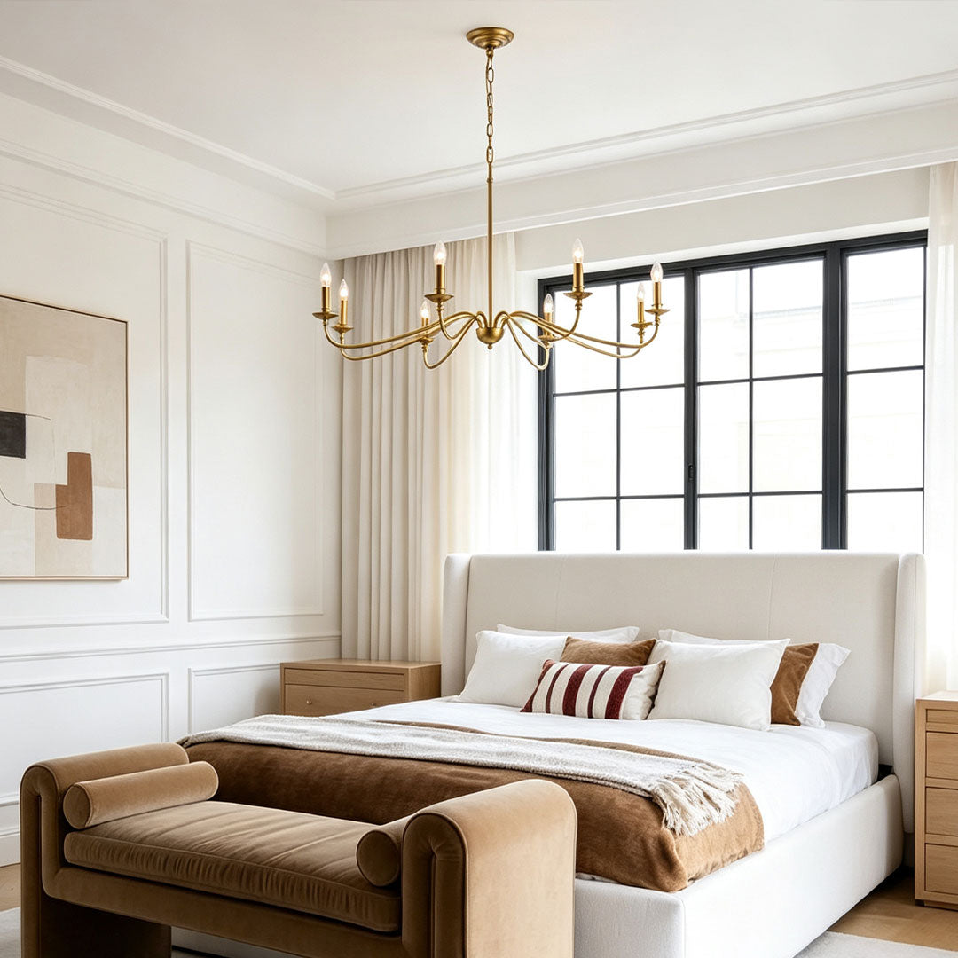 Modern brass chandelier installed above a contemporary bedroom with warm minimalist interior styling.