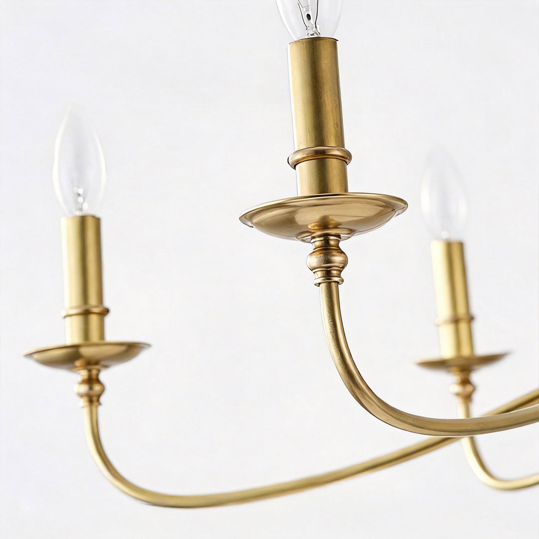 Modern brass chandelier close-up featuring curved candle arms and brushed brass finish details.