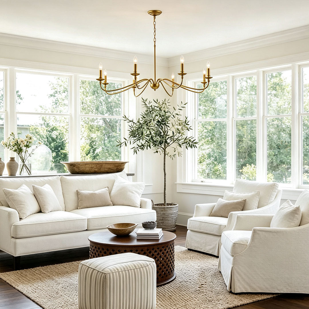 Modern brass chandelier styled in a sunlit living room with elegant neutral-toned furniture.