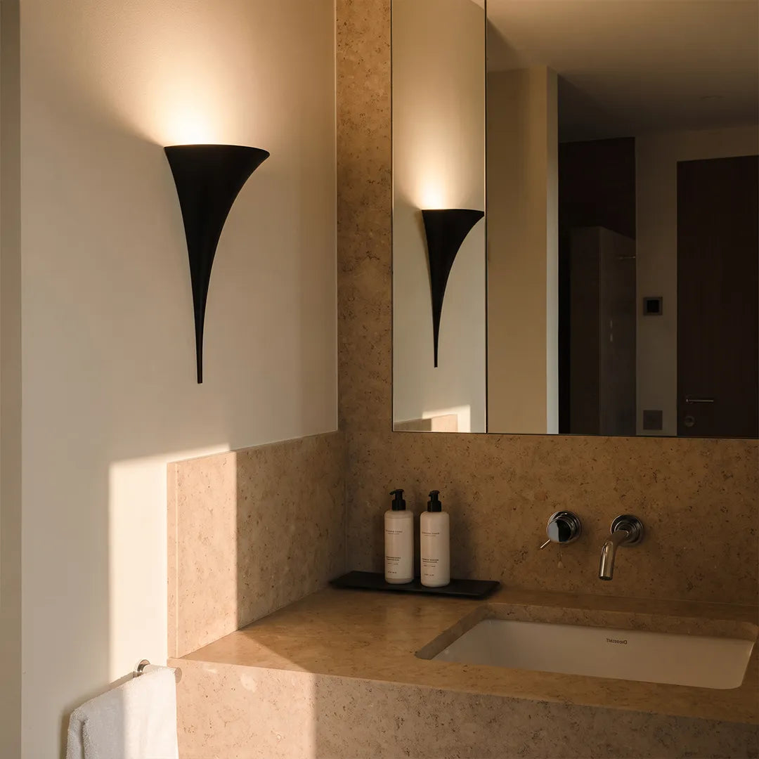 Modern brass wall sconce in a black finish mounted beside a bathroom mirror above a stone vanity.