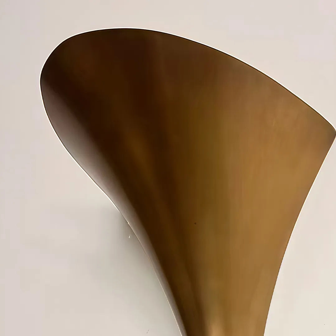 Modern brass wall sconce close-up showing the flared cone shade and sculptural tapered silhouette.