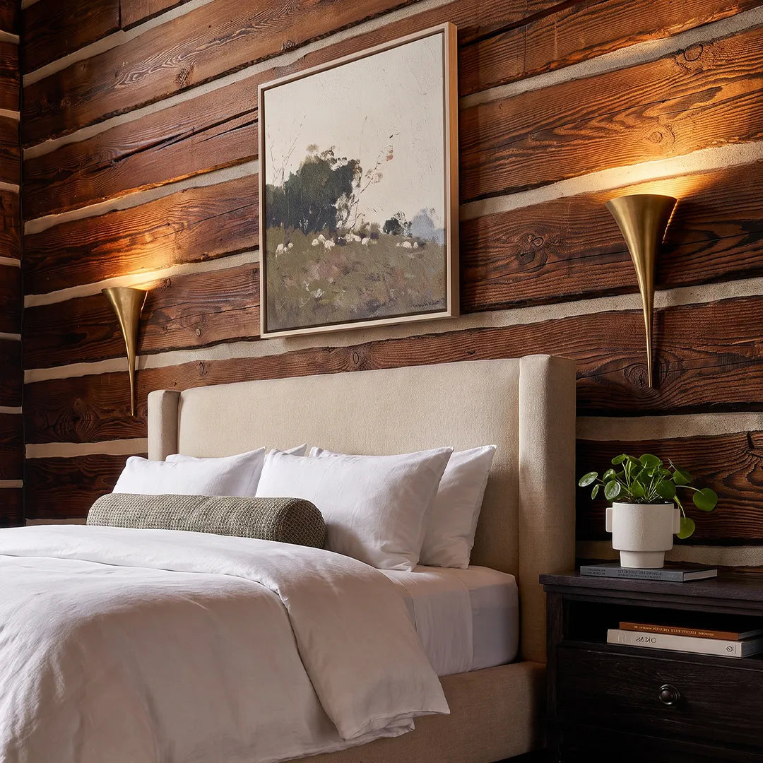 Modern brass wall sconce mounted above a nightstand in a contemporary bedroom with wood plank walls.