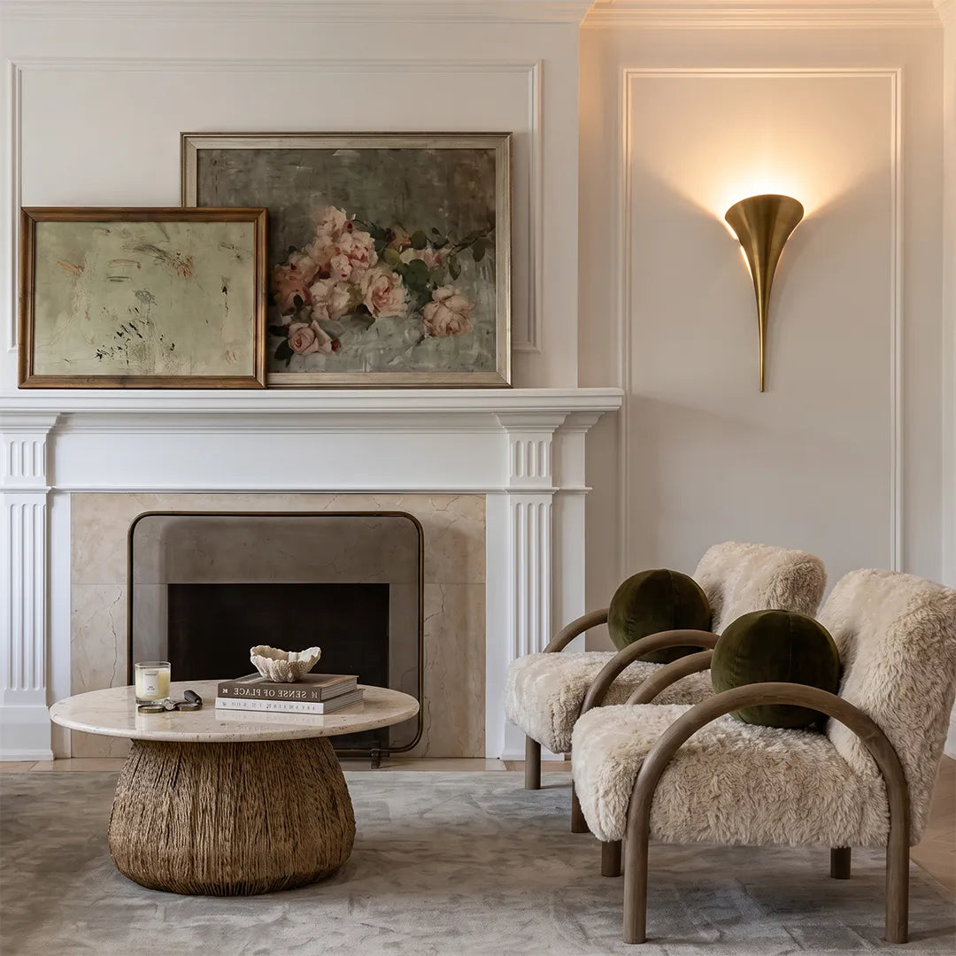 Modern brass wall sconce installed beside a fireplace in a cozy living room with neutral decor.