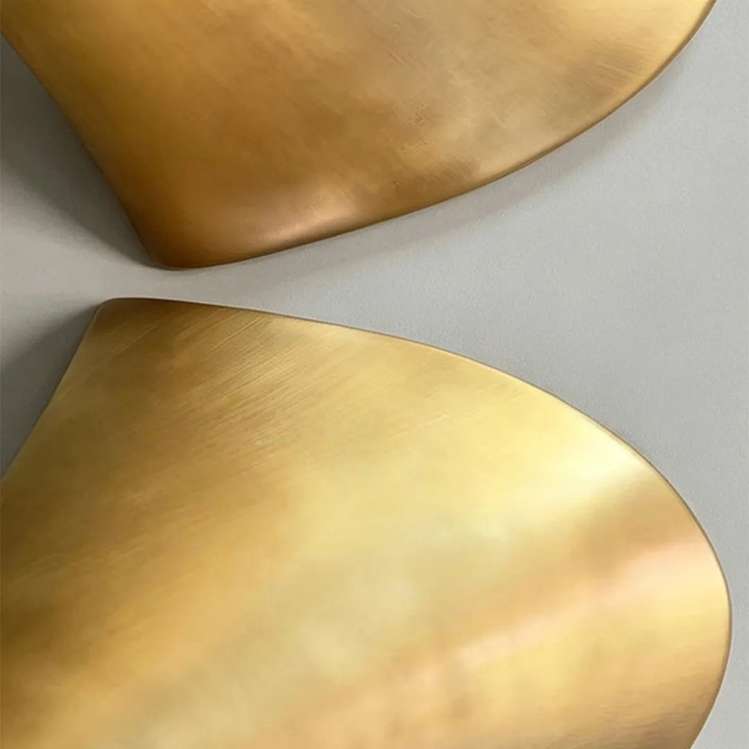 Modern brass wall sconce detail showing the smooth metallic finish and curved sculptural form.