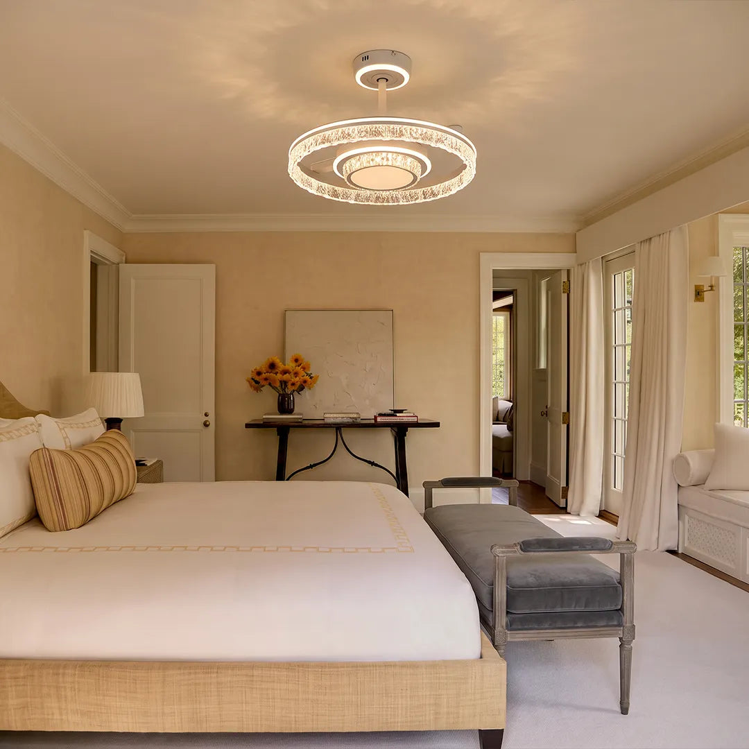 Modern ceiling fan with lights installed in a bright bedroom with neutral decor and warm crystal ring illumination.